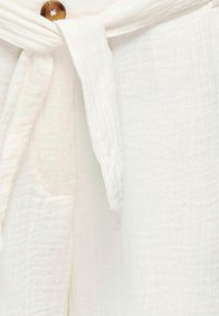 Bijela teksturirana tkanina s detaljem vezane trake i smešnim dugmetom. Materijal izgleda mekano i lagano, s blagim naborima.