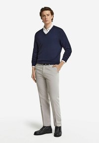 Marinblå tröja med V-ringning, ljusgrå byxor och svarta ankelstövlar. Outfitten har en mjuk textur och en klassisk passform.