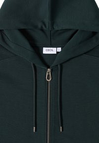Felpa con zip di colore verde scuro, dotata di cordoncino, con una texture liscia e una zip argentata. L'etichetta riporta la scritta "CECI" su un tag rettangolare bianco.