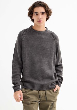 Suéter de punto gris oscuro con cuello redondo, puños y dobladillo acanalados, con mangas raglán y una textura suave. Combinado con pantalones olivas.
