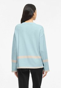 Pull bleu clair à manches longues, col large, et rayures horizontales beiges en bas. Matière douce et coupe décontractée.