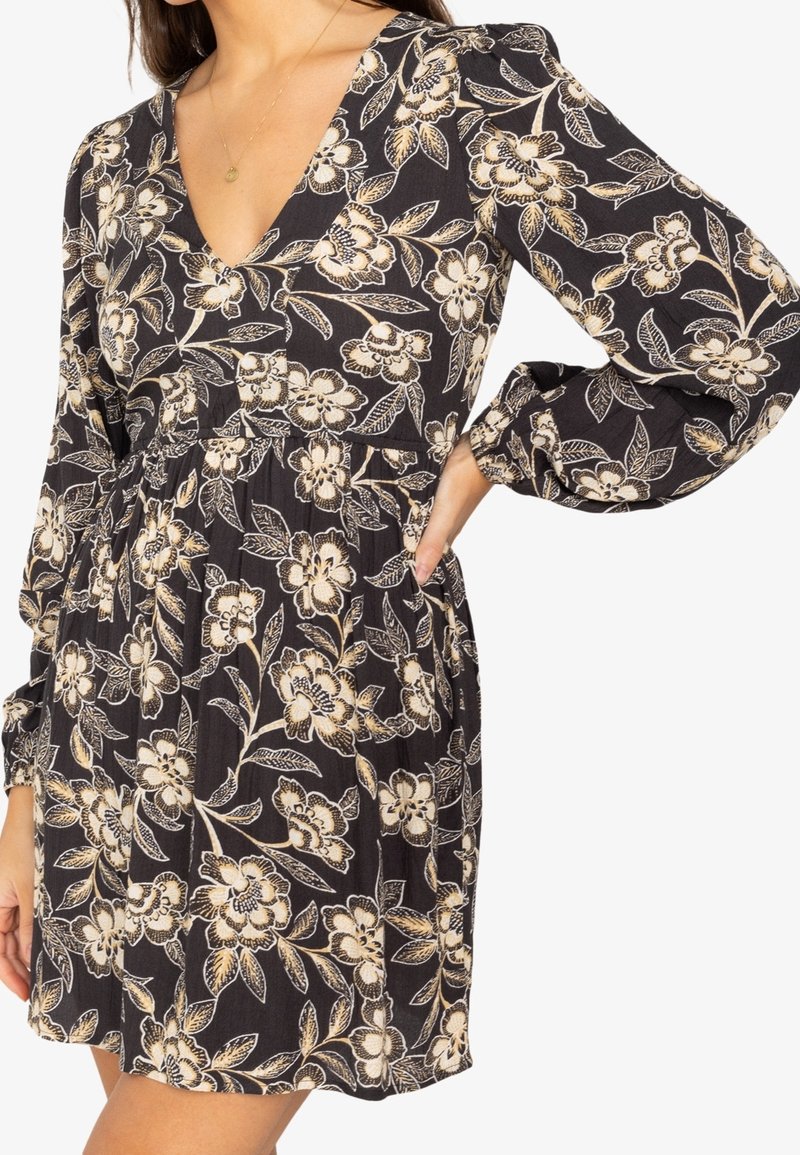 Vestido negro con un patrón floral en crema y oro, con escote en V, mangas largas abullonadas y una cintura ajustada con una falda acampanada.