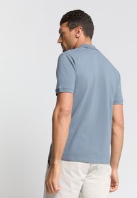 Heren poloshirt in lichtblauw, korte mouwen, zachte textuur, standaard kraag, achterkant, minimalistisch ontwerp, strakke lijnen.