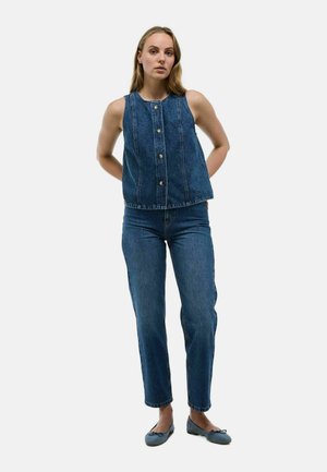 Débardeur en denim sans manches avec fermeture à boutons sur le devant, associé à un jean en denim taille haute. Les deux sont de couleur bleu foncé avec une texture lisse et nette.