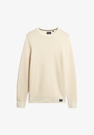 Sweter z wafelkowej dzianiny w kolorze kremowym, z okrągłym dekoltem i długimi rękawami. Posiada ribbowany dół i małą metkę z logo na dole.