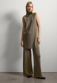 Conjunto de punto de gran tamaño en color marrón metálico, que incluye una blusa sin mangas con cuello alto y pantalones de pierna ancha con textura acanalada y detalles en contraste.