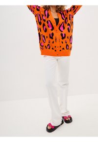 Orange leopard print cardigan with pink accents, black buttons, paired with white pants and black platform sandals featuring pink straps.