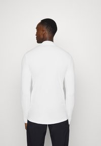 Long-sleeve white shirt with a smooth texture and a fitted design, featuring a high collar and seamless cuffs.