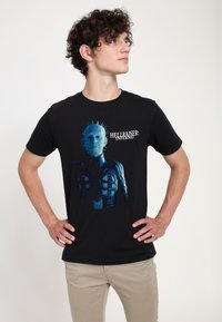 Sort bomulds T-shirt med en blå grafik af en karakter fra "Hellraiser: Inferno," med indviklede ansigtstræk og vinklede designs.