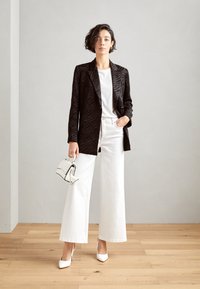 Svart zebra-randig blazer över en vit t-shirt, parat med vita vida jeans och vita spetsiga klackar, hållande en liten vit handväska.