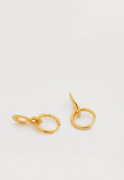 Pereche de cercei mici aurii, de tip cerc, cu tije curbate abstract, pe un fundal alb.