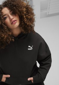 Felpa con cappuccio nera realizzata in tessuto morbido con vestibilità comoda. Presenta un grande logo Puma bianco sul petto e una tasca a marsupio sul davanti.