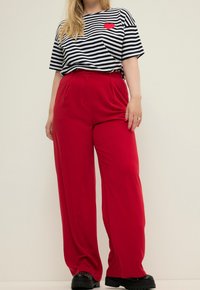 Czarnobiała pasiasta koszulka z naszywką w kształcie czerwonego serca, zestawiona z czerwonymi, szerokimi spodniami z wysokim stanem oraz czarnymi masywnymi butami.