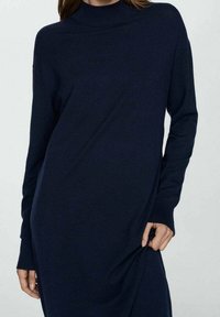 Vestido de punto azul marino con cuello alto, mangas largas y un ajuste relajado. Presenta puños acanalados y aberturas laterales para facilitar el movimiento.