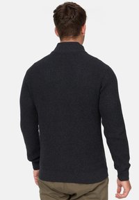Mørkegrå strikkegenser med høy krage, teksturert stoff og ribbestrikkede mansjetter. Bakfra viser den en tettsittende design og sømløs konstruksjon.