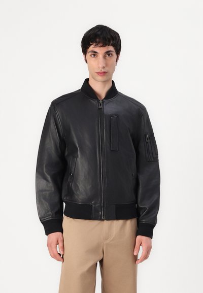 Veste bomber en cuir noir avec une fermeture éclair à l'avant, des poignets côtelés et une poche sur la manche gauche ; texture lisse et coupe classique.