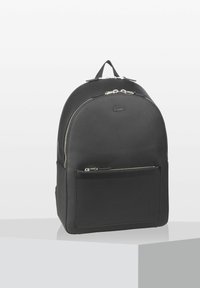 Svart ryggsäck med texturerat material, rundad topp, framficka med blixtlås och silverfärgade detaljer. Lacoste-logotyp präglad på framsidan.