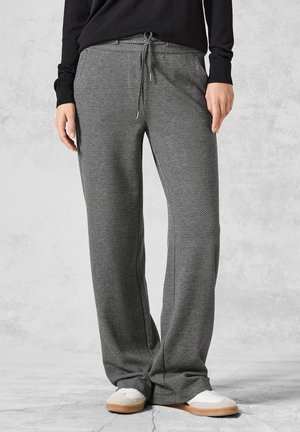 Personne portant un pantalon large à motif chevron gris et noir avec une taille à cordon et des baskets blanches avec des semelles beige.