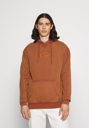 Brauner Hoodie mit einer Kängurutasche, Kapuze mit Kordelzug und strukturiertem Patch auf der Brust. Mit gerippten Bündchen und lockerer Passform.
