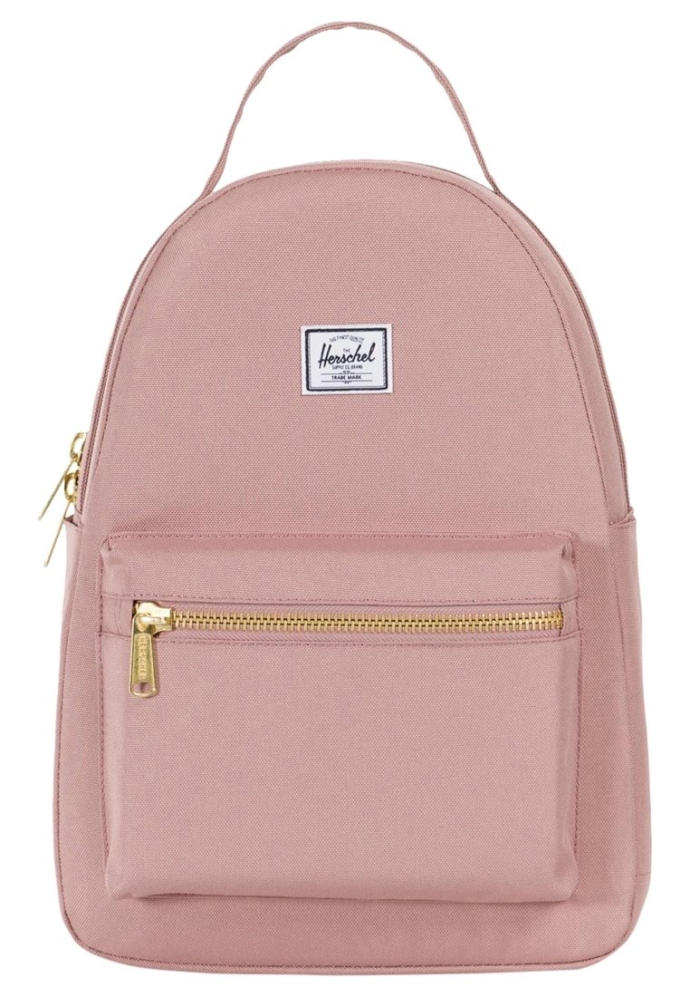 Jasnoróżowy plecak wykonany z płótna. O zaokrąglonym kształcie z przednią kieszenią na zamek. Posiada biały naszywkę z logo oraz złote elementy zamka.