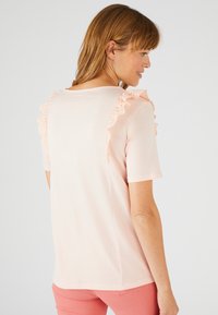 Camiseta de manga corta rosa claro con detalles de volantes de encaje a lo largo de los hombros. Textura suave, ajuste relajado y cuello redondo.