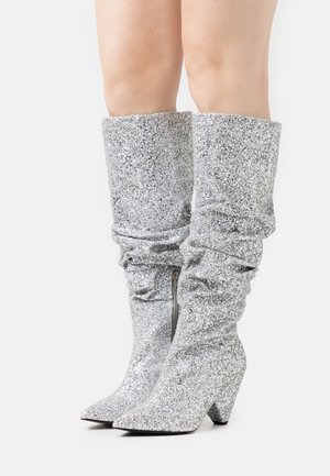 Bottes montantes en paillettes argentées avec un design décontracté, une pointe pointue et un talon en bloc. Comprend une fermeture éclair latérale et une surface texturée.