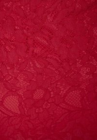 Tissu en dentelle rouge avec des motifs floraux, présentant une texture délicate et un design complexe. Apparence en couches avec des sections semi-translucides.