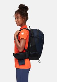 Zaino nero e blu con scomparti multipli, spallacci regolabili e una tasca frontale. Indossato con una maglietta arancione e pantaloni blu.