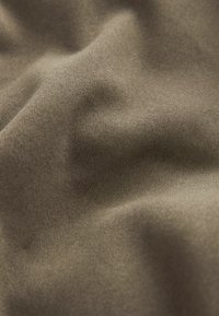 Tessuto khaki con una superficie liscia e testurizzata, caratterizzato da pieghe sottili e un colore uniforme, che mette in risalto un materiale morbido e flessibile.