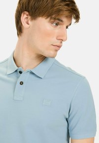 Lichtblauw poloshirt van structuurstof, met een klassieke kraag, twee knopen en een subtiele logo op de borst.