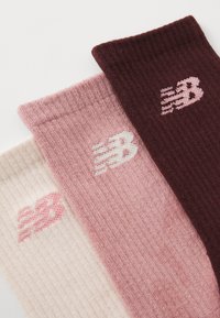 Drei Paar gestrickte Socken in Hellrosa, Rosa und Dunkelburgunder. Jede hat ein Logo mit einem stilisierten "N" in kontrastierenden Farben.