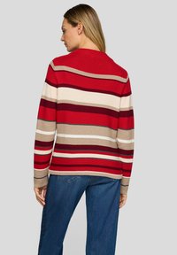 Roter und beiger gestreifter Pullover mit gerippter Struktur und Rundhalsausschnitt, kombiniert mit blauen Jeans. Rückansicht mit unterschiedlich breiten Streifen.