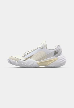 Zapatilla deportiva blanca con paneles de malla texturizada, diseño minimalista, acentos dorados y suela de goma con un patrón en zigzag para mayor tracción.