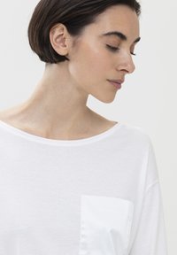 Witte katoenen T-shirt met een wijde halslijn, met een glanzend, wit satijnen borstzakje. Zachte textuur, ontspannen pasvorm, eenvoudig design.
