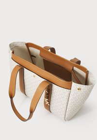 Grand sac fourre-tout avec un extérieur en tissu beige au design imprimé, des anses en cuir marron et un compartiment central zippé.