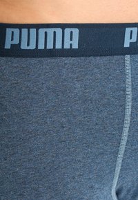 Boxers oscuros de color azul con una textura de tela suave, que cuentan con una amplia cinturilla elástica con la marca "PUMA" en un azul más claro que contrasta.