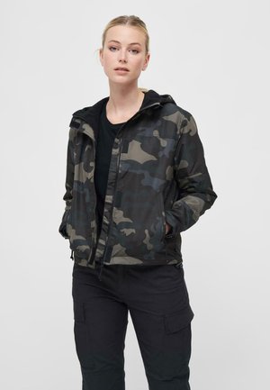 Camouflage jacket in dark green and gray tones, featuring a hood, zip front, and side pockets, paired with black cargo pants.