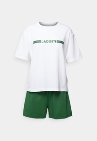 T-shirt en coton blanc avec logo et rayures "LACOSTE" verts, associée à un short en coton vert. Coupe décontractée, manches courtes, design simple.