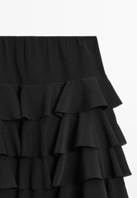 Jupe noire à volants avec plusieurs niveaux, faite de tissu plissé. Présente une large ceinture élastique et une finition texturée.