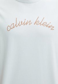 Jasnoniebieski bawełniany t-shirt z haftem w stylu kursywy "calvin klein" w kolorze brzoskwiniowym na wysokości klatki piersiowej. Miękka tekstura, klasyczny okrągły dekolt.