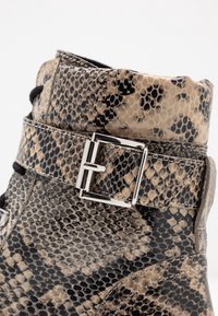 Bottine en cuir façon peau de serpent noir et beige avec une finition texturée, dotée d'une boucle métallique et d'un design à lacets.