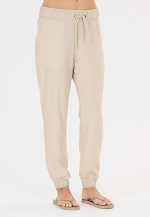 Lysebeige joggingbukser med elastisk talje og snøre, båret med beige flip-flops på bare fødder, vist fra talje til fødder.