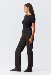 Zwart aansluitend T-shirt met korte mouwen en een ronde halslijn, gecombineerd met hoge zwarte rechte jeans, van een textuurstof en minimale details.