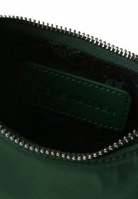 Zielony woreczek z tkaniny o teksturowanej powierzchni, z zamkiem błyskawicznym w kolorze srebrnym oraz wytłoczonym napisem wewnątrz, który brzmi "STEVE MADDEN."