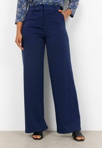 Navy wide-leg trousers with a smooth texture, tailored waist, front pockets, and pleats. Paired with black open-toe heels.