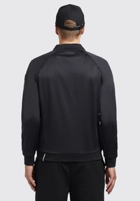 Giacca atletica nera con una texture liscia, maniche raglan e un berretto nero a contrasto. Presenta un piccolo logo sul colletto.