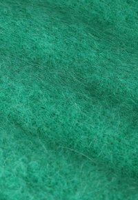 Tissu en feutre vert avec une texture douce et moelleuse, présentant une couleur uniforme et de subtiles variations d'épaisseur des fibres.