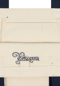 Τσάντα από μουσαμά σε κρέμ χρώμα με μπλε-ναυτικό λουριά, με κεντημένο λογότυπο και ασημί D-ring στερέωση. Υφή υφάσματος με ορατή ραφή.