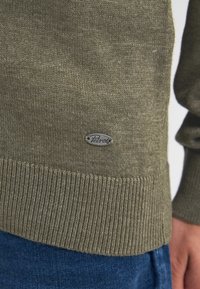 Olive'owy sweter z ściągaczem u dołu i przy rękawach, wykonany z mieszanki bawełny, z małą srebrną naszywką z logo przy dolnej krawędzi.