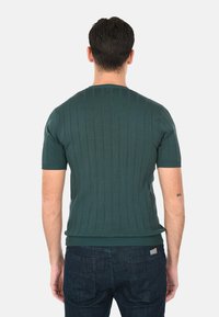 Maglione verde a maniche corte, in maglia a coste, con scollatura rotonda e silhouette aderente, abbinato a jeans scuri.